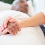 A comforting gesture as a hand holds another in a hospital setting, symbolizing care and support.